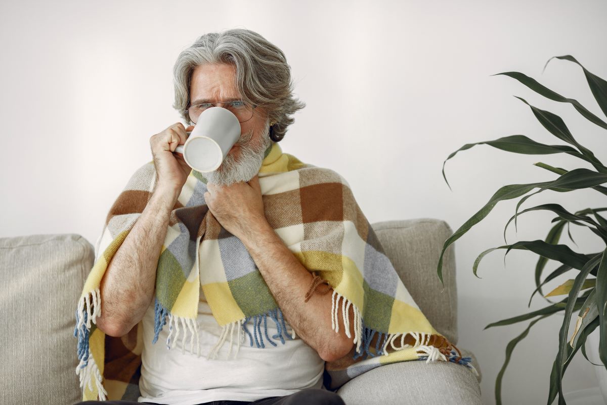 staršímu muži zabalenému do deky je zima, pije teplá nápoj